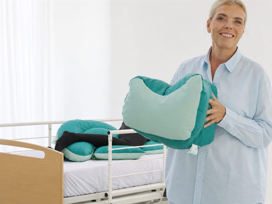 Malene holding an NG Positioning Cushion beside a demonstration bed.