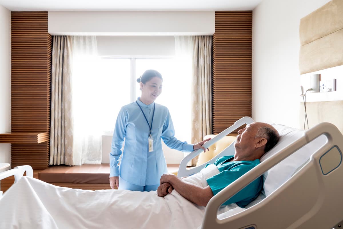 A caregiver speaking with a resident resting in a care bed