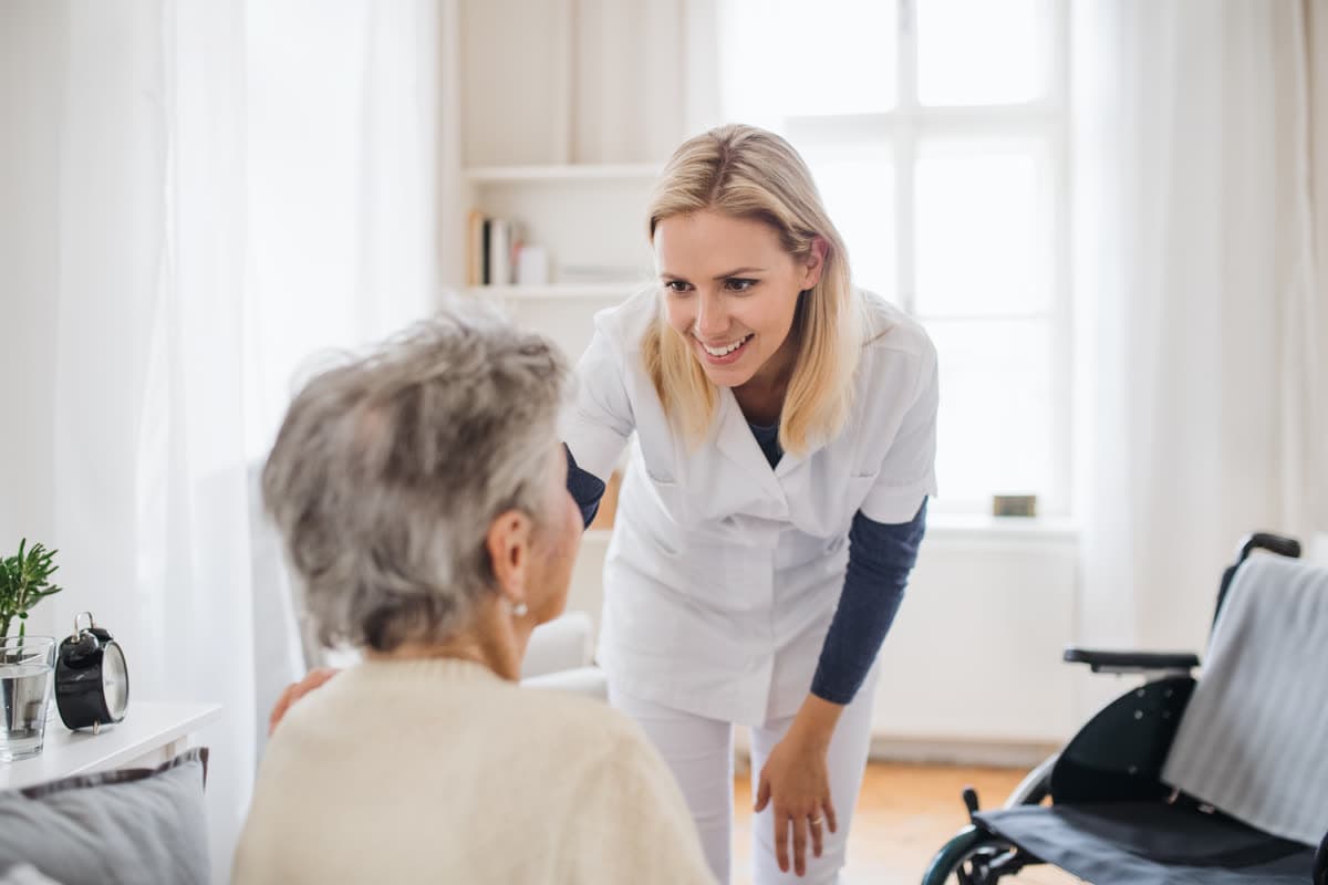 A caregiver speaking with a seated older adult, wheelchair nearby