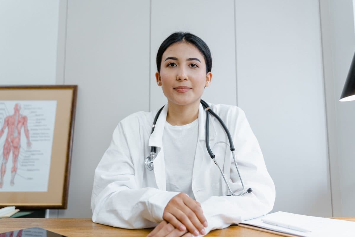 A clinician in a white coat and stethoscope seated at a desk