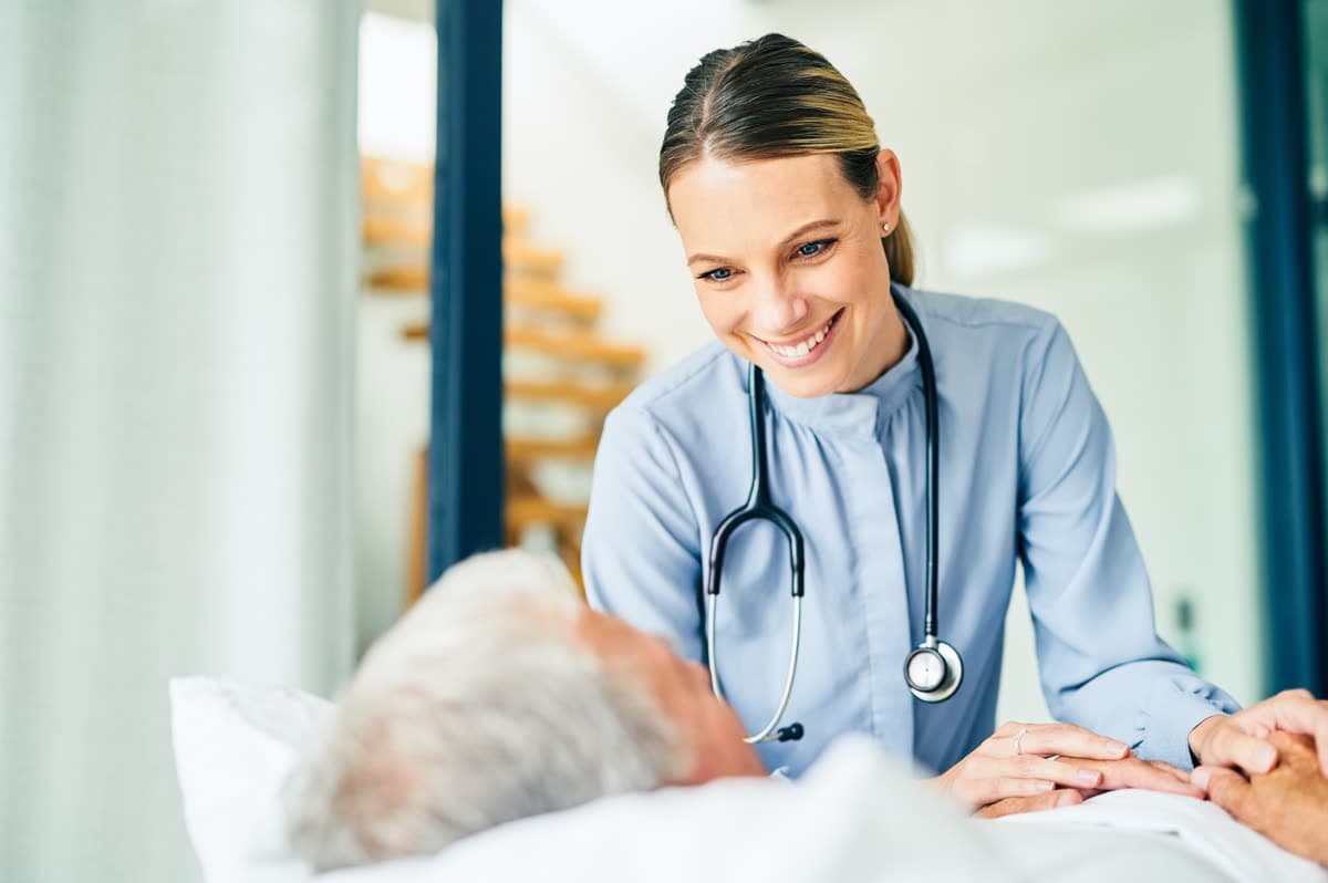 A nurse at the bedside holding a resident’s hand
