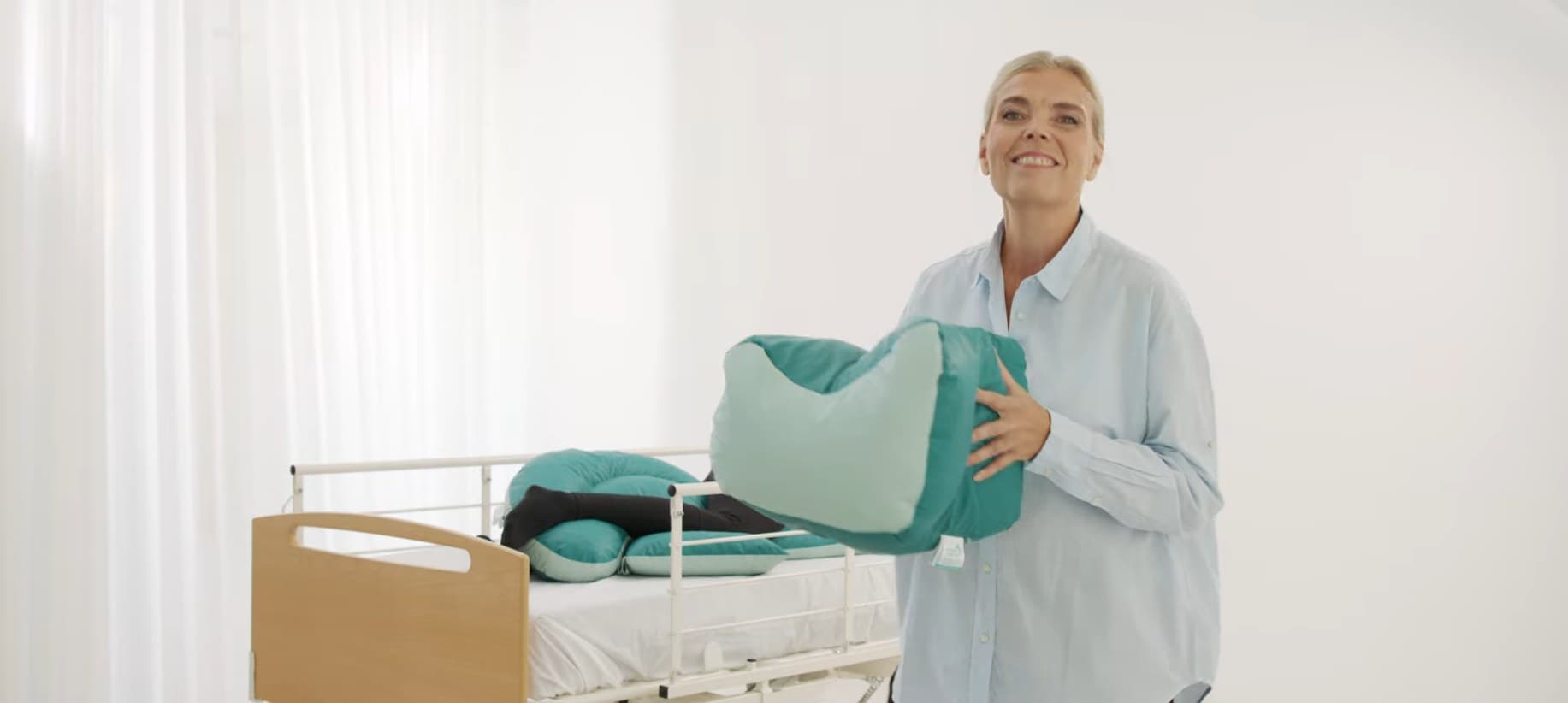 A clinical educator holding a shapeable positioning support beside a care bed