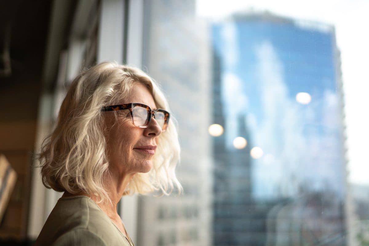 A woman in glasses looking out of an office window